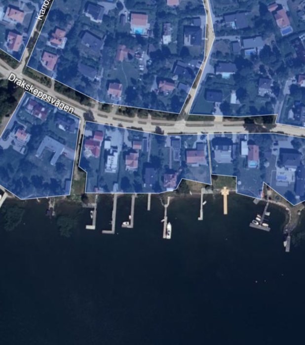 Satellitbild över en strandtomt med bryggor och båtar vid kustnära bostäder.