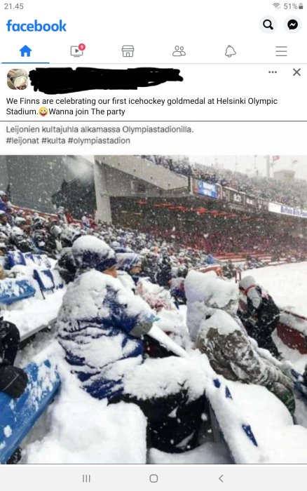 Publik klädd i blått och vitt firar under snöfall på en idrottsarena.