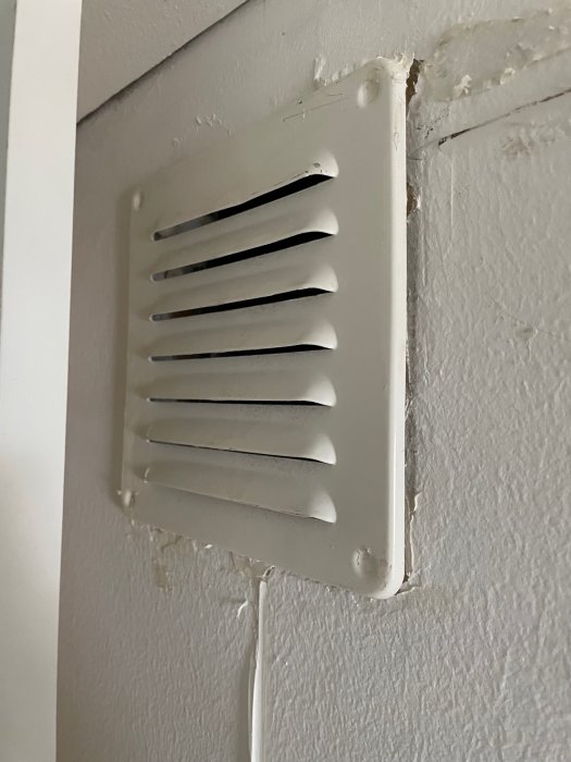 Ventilationsgaller på vägg med sladd hängande undan, tecken på renovering syns.