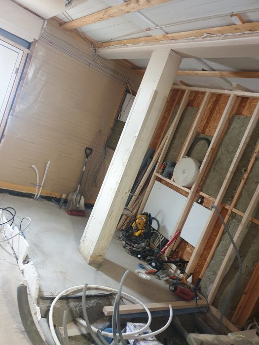 Pågående byggprojekt med nymonterade reglar och isolering i ett rum, verktyg utspridda på golvet.