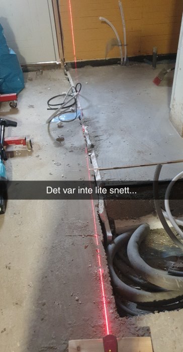 Byggarbetsplats med ojämnt skuren matta och laserlinje som visar ojämnheter på golvet.