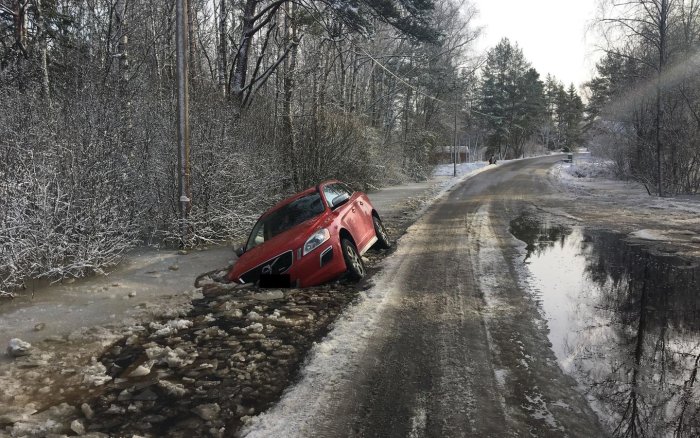 Bil fast i vattenfyllt dike vid översvämmad väg med frostiga träd.