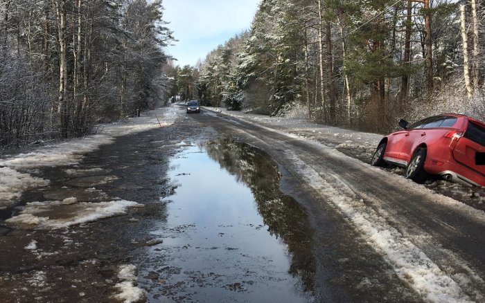 Bil fast i vattenfyllt dike bredvid översvämmad väg med snö och is.