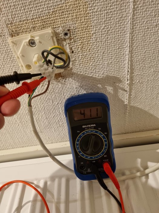 Multimeter visar 411 volt vid mätning av elektrisk installation för radiator.