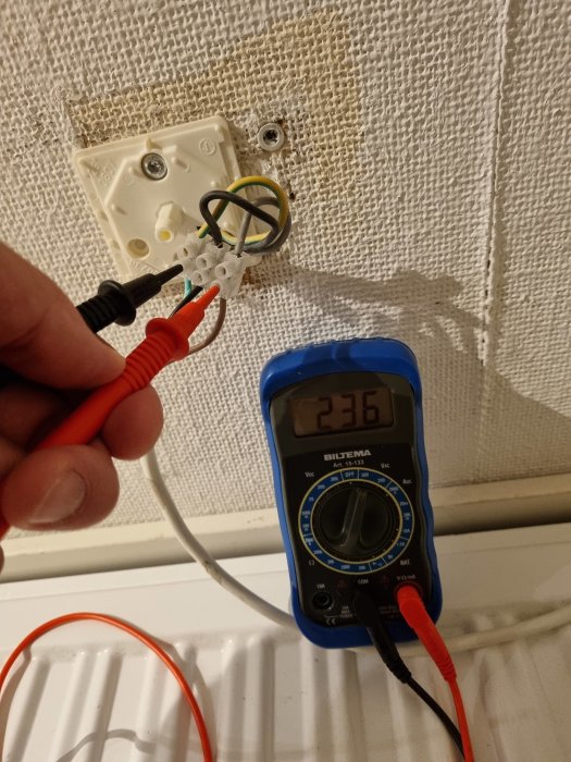 Mätning av spänning med en multimeter som visar 236V på en radiatorinstallation.