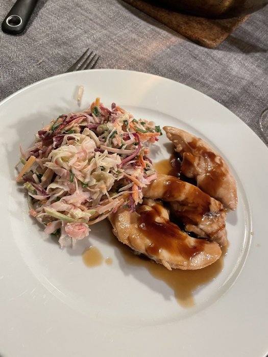 Hoisinkyckling och färgrik gari-slaw på en vit tallrik, serverat på ett dukat bord.