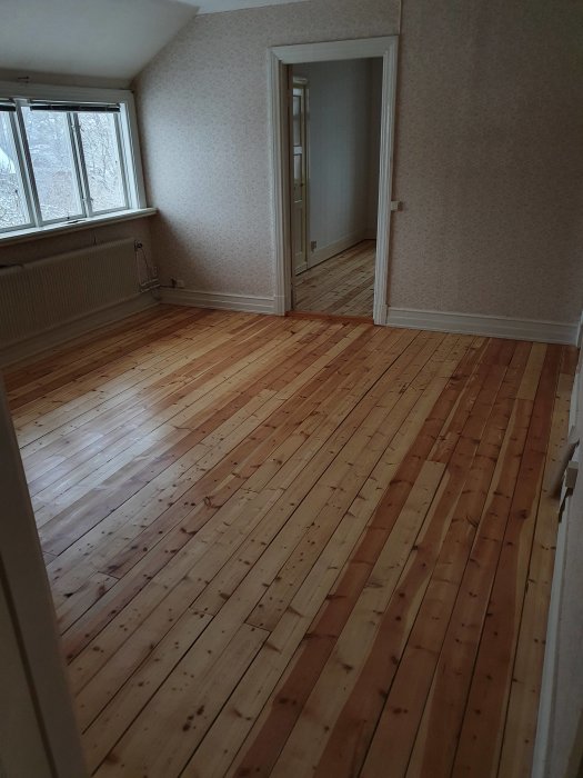 Nyslipat trägolv med sidenmatt finish i ett rum med tapetväggar och öppen dörr.