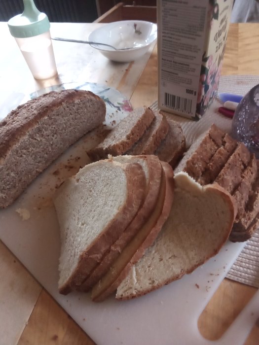 Skivat rågbröd och vetebröd på skärbräda, mjölkflaska och tom skål i bakgrunden.