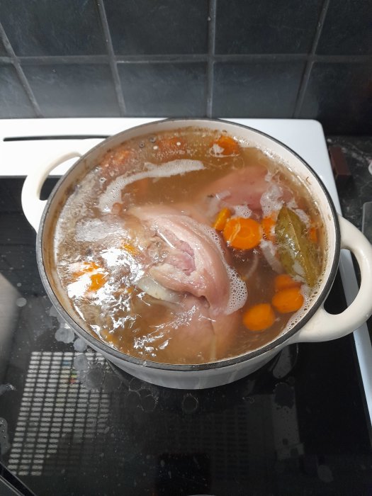 En fläsklägg kokas med morötter och kryddor i en stor gryta på spisen.