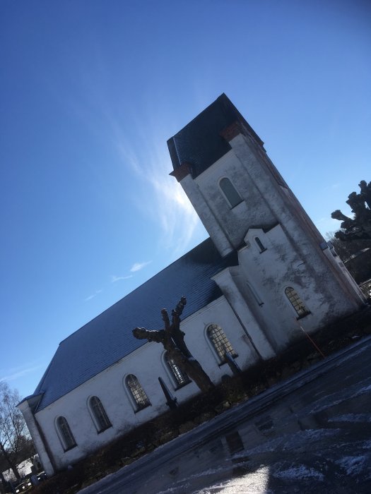 Svensköps Kyrka badad i vårsol med snöfläckar på marken, mot en klarblå himmel i Killhult, Skåne.