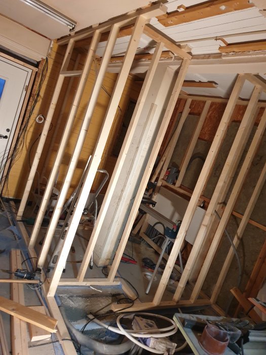 Delvis uppbyggda träreglar i ett pågående inomhusbyggprojekt med isolering och verktyg synliga.