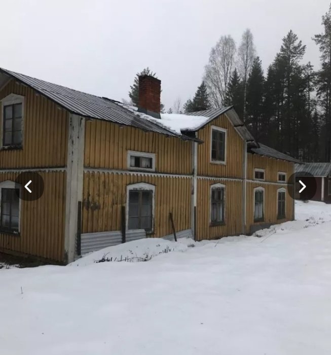 Äldre gult trähus med två våningar och snö på taket och framför, med tanke på försiktig rivning för återanvändning.