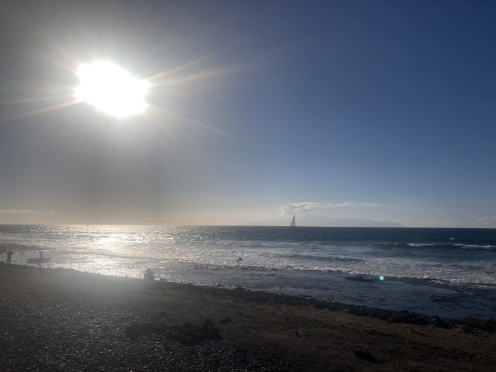 Solnedgång över havet med silhuetter av personer och segelbåt i bakgrunden.