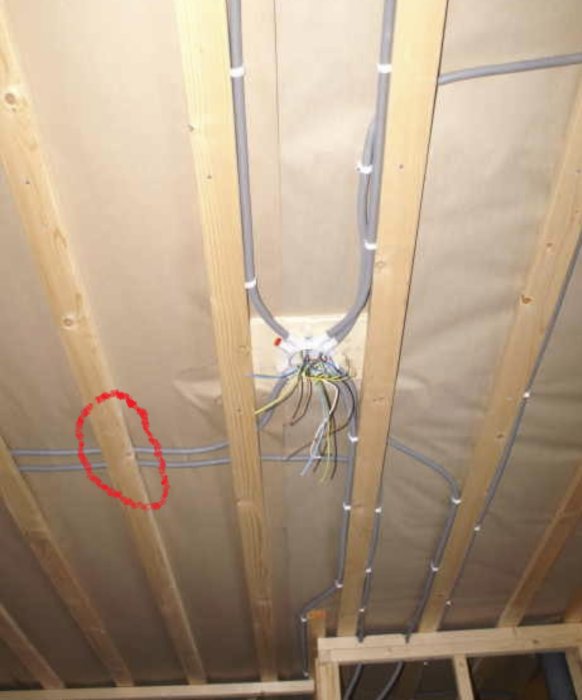 Inre struktur av en vägg med trästommar, isolering, elektriska kablar och rör markerade med röd cirkel.