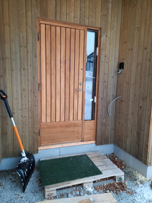 60-tals teakdörr i nybyggd villa, snöskyffel bredvid, dörren behöver oljas, på trappa av trä.
