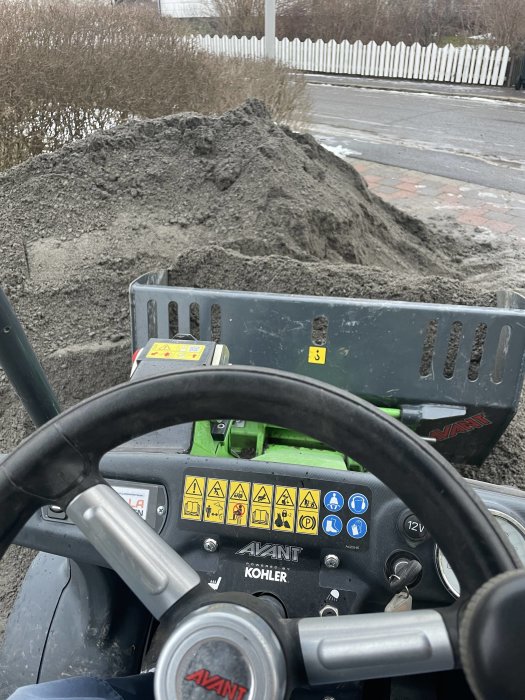 Vy från förarsätet av en Avant-minilastare med snö och smutsig hög framför i grått väder.
