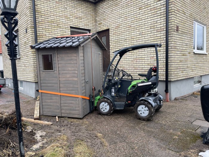 Ett litet förråd med tjärpappstak och en ATV parkerad bredvid, på en blöt och delvis snötäckt mark.