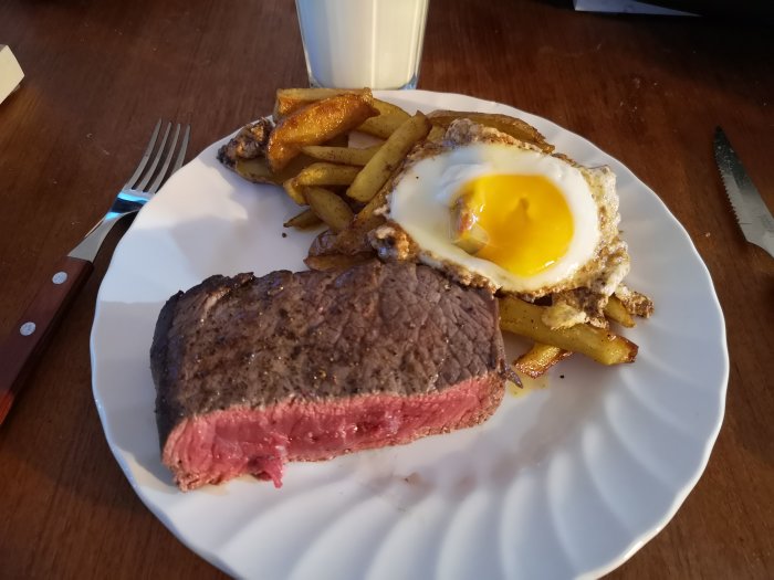En tallrik med medium stekt biff, stekt ägg och pommes frites, med kniv och gaffel.