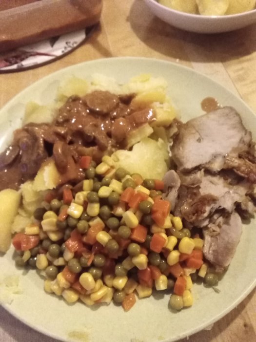 Helstekt karré med plommonsås, tomatpuré, champinjoner, kokt potatis och blandade grönsaker på tallrik.