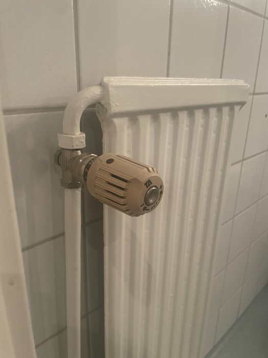 Vattenburnt radiatorselement i badrum med termostatventil och vita kakelväggar.