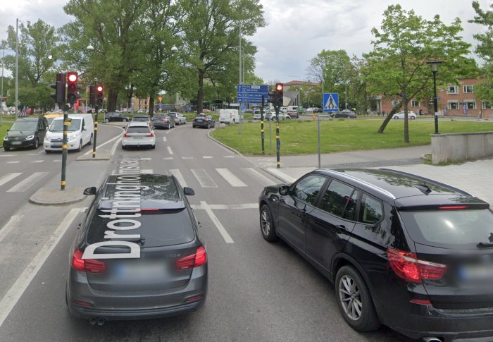 Bilar i kö vid rött ljus nära en rondell med tydlig väjningspliktmarkering.