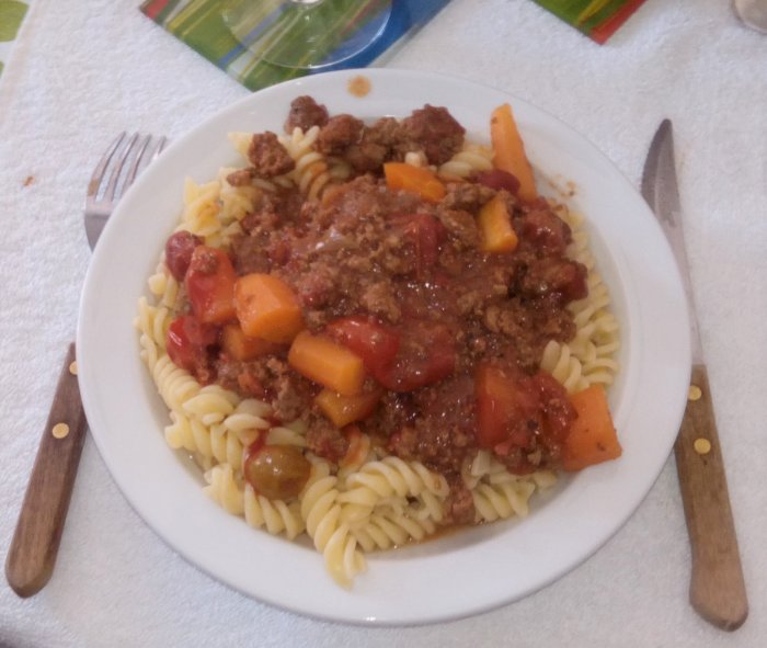 Tallrik med pasta och köttfärssås, bestående av fusilli, köttfärs och tomat, med gaffel och kniv.
