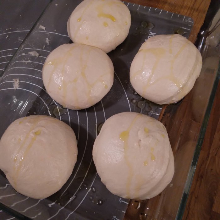 Förjästa pizzadegsbollar med olivolja på ett ugnsfast glasfat.