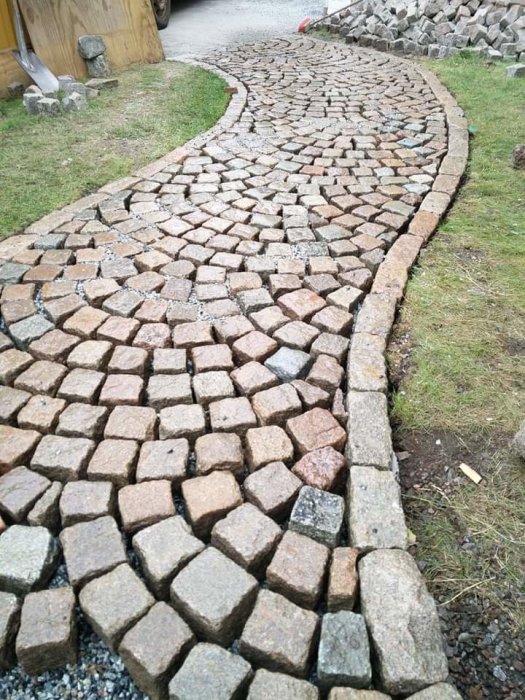 Gångväg med oregelbundet lagda, patinerade gatstenar i natursten och granit som skapar ett rustikt utseende.