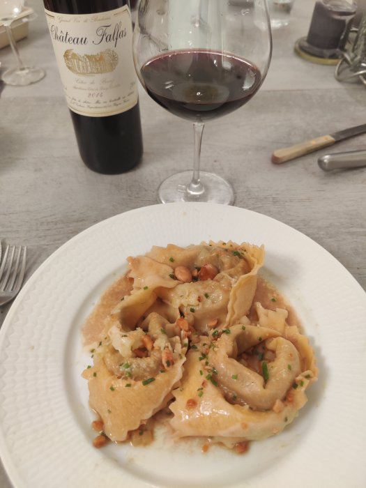 Tallrik med tortellini och strössel av örter bredvid ett glas rödvin och vinflaska.