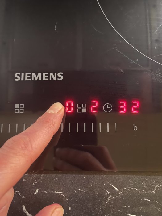 Finger pekar på felkod E 0232 på en Siemens spishäll med en delvis synlig reflektion av personen som tar bilden.