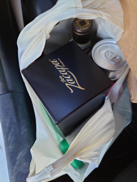 Plastpåse med vinflaska, presentask och burkdricka i bilens fotutrymme.