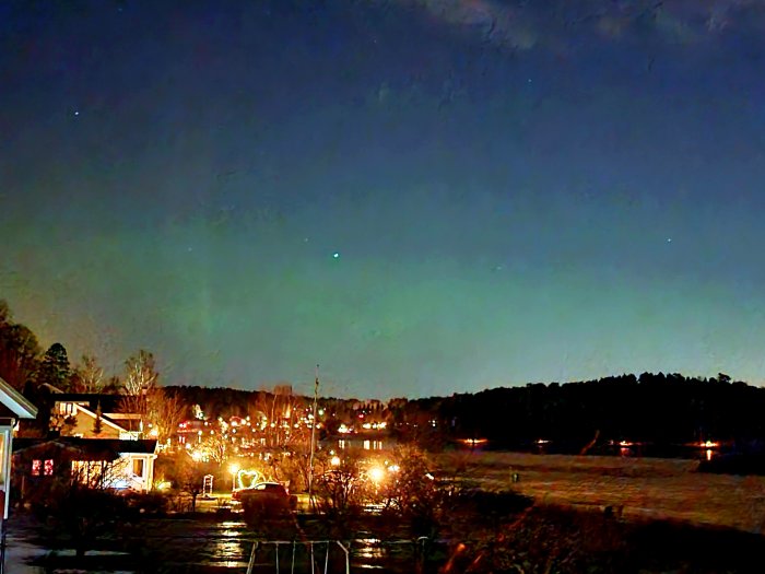 Nattbild av ett bostadsområde med hus som upplysts av gatulampor och en stjärnklar himmel ovanför.