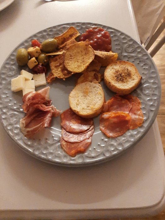Tapastallrik med chorizo, pata negra, manchegoost, oliver med mandel, rostade baguette skivor och nachos.