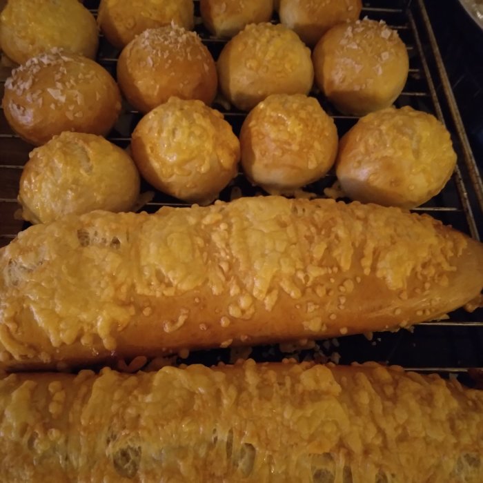 Nybakade frallor och en limpa med ost på en ugnsplåt.