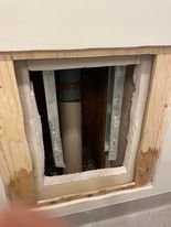 Öppning i vägg med exponerade rör och isoleringsmaterial bakom en avlägsnad plywoodskiva.
