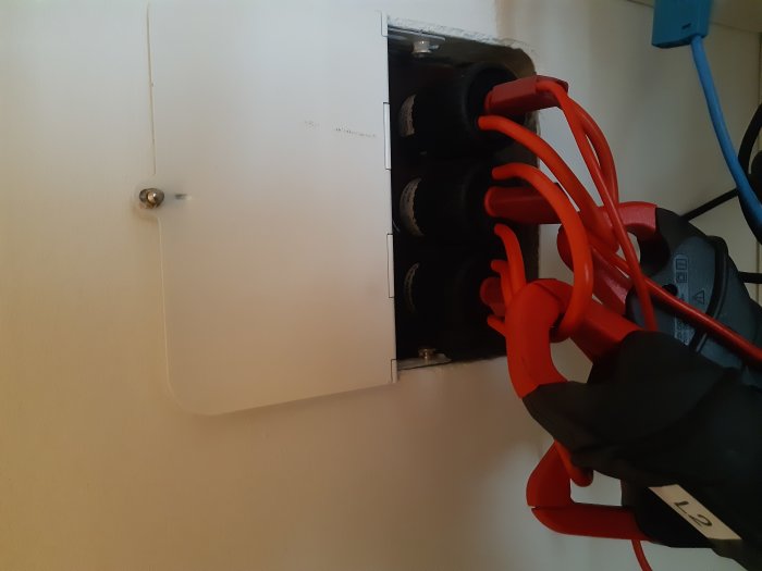 Elmätare med påkopplade mätinstrument och röda kablar, röd diod lyser.