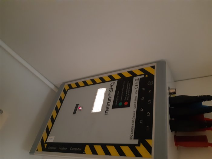 Elkvalitetsmätare med tänd röd diod indikerande kvalitetsavvikelser, ansluten med kablar.