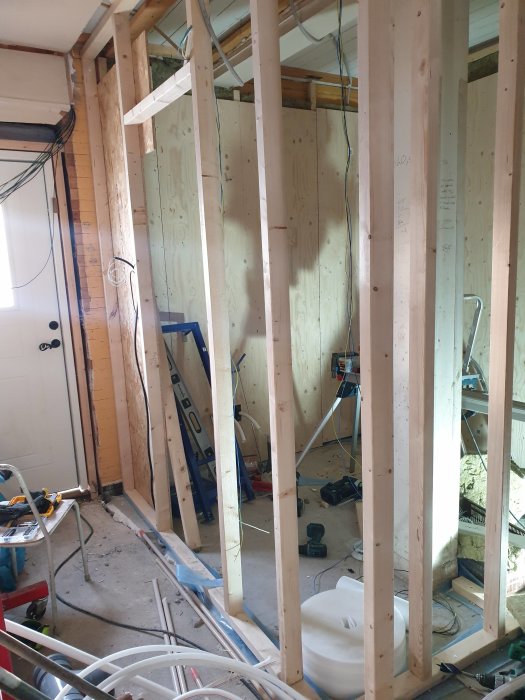 Byggarbetsplats med plywood på väggar, träreglar, verktyg och byggmaterial på golvet.