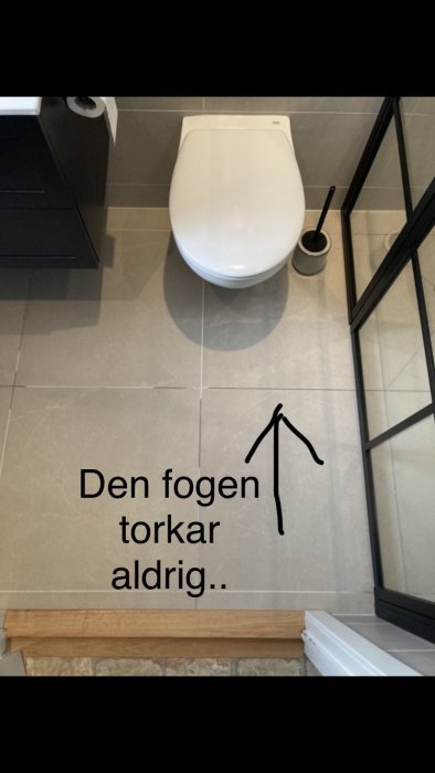 Ett nyrenoverat badrum med storformat kakel, en toalett och duschdörr, visande en fuktig fog som inte torkar.