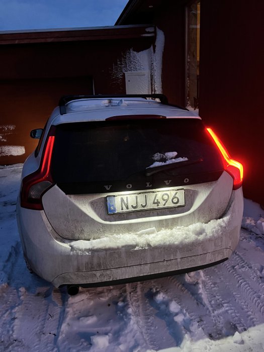 En smutsig Volvo bil parkerad i snö med fungerande bakljus på kvällen.