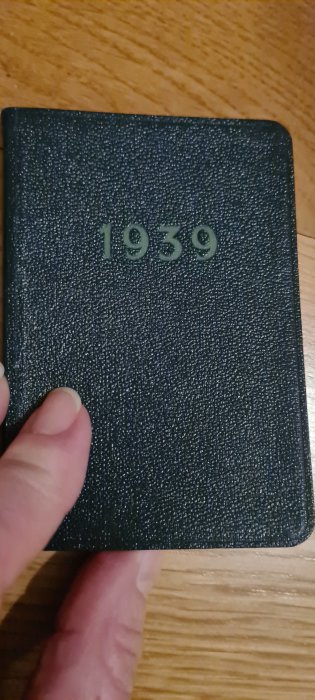 Hand håller en svart bok med siffrorna 1939 präglade på framsidan.