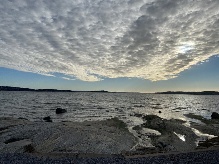 Klippstrand vid havet under en dramatisk molnhimmel vid solnedgång.