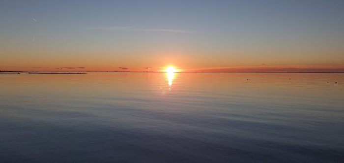 Solnedgång över stilla hav med reflektioner av solen på vattenytan och klart himmel.