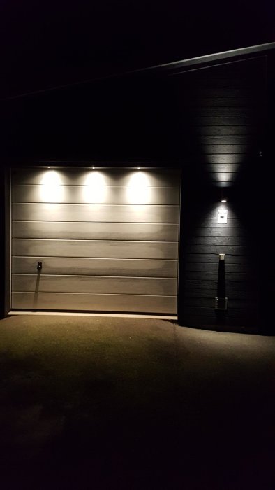 Garageport upplyst av tre takspottar med dold installation, matchande färg mot mörk panel.