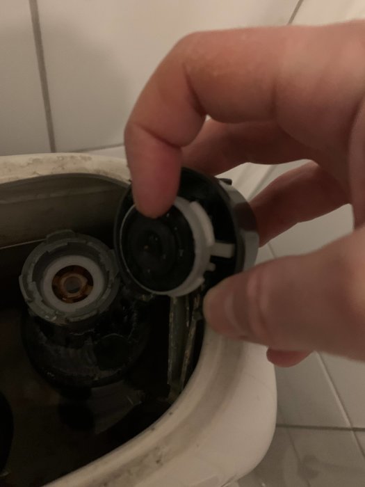 Hand visar en svart gummipackning och toalettens inre mekanism där det rinner över.