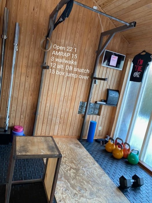Hemmagym med träningsutrustning såsom kettlebells, hantlar, träningsbox och ringar, samt träningsplan på väggen.