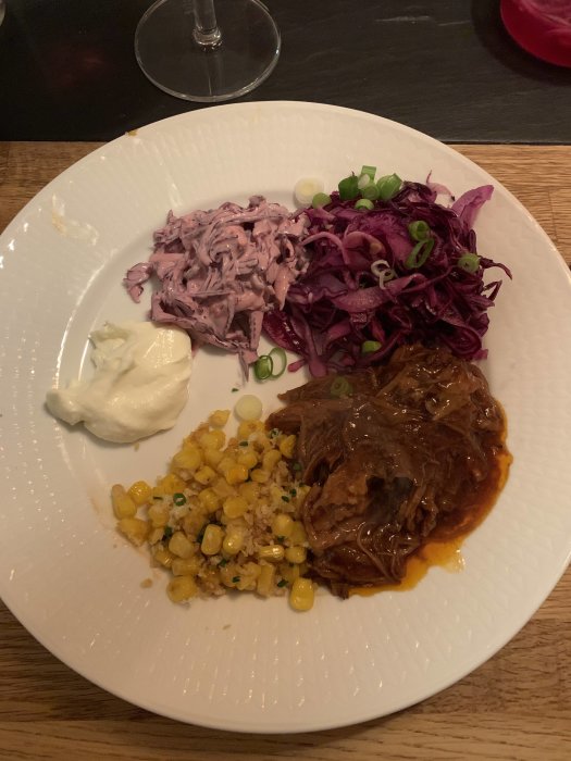 Tallrik med pulled pork, rödkålssallad, majs och crème fraîche, utan synliga tortillabröd.