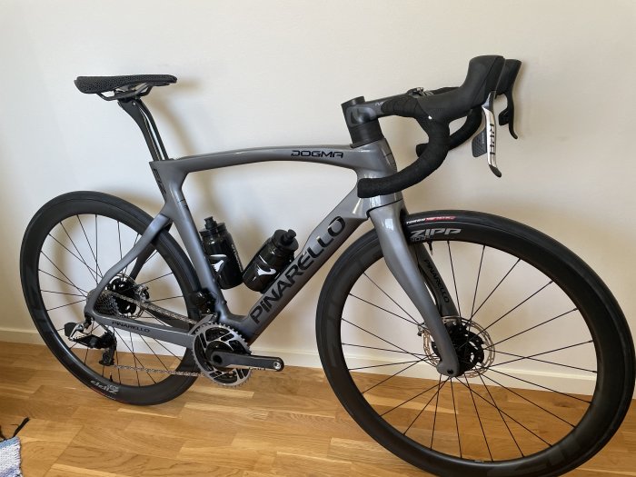 Pinarello Dogma F12 racercykel parkerad inomhus med ZIPP-hjul och svart-grått färgschema.