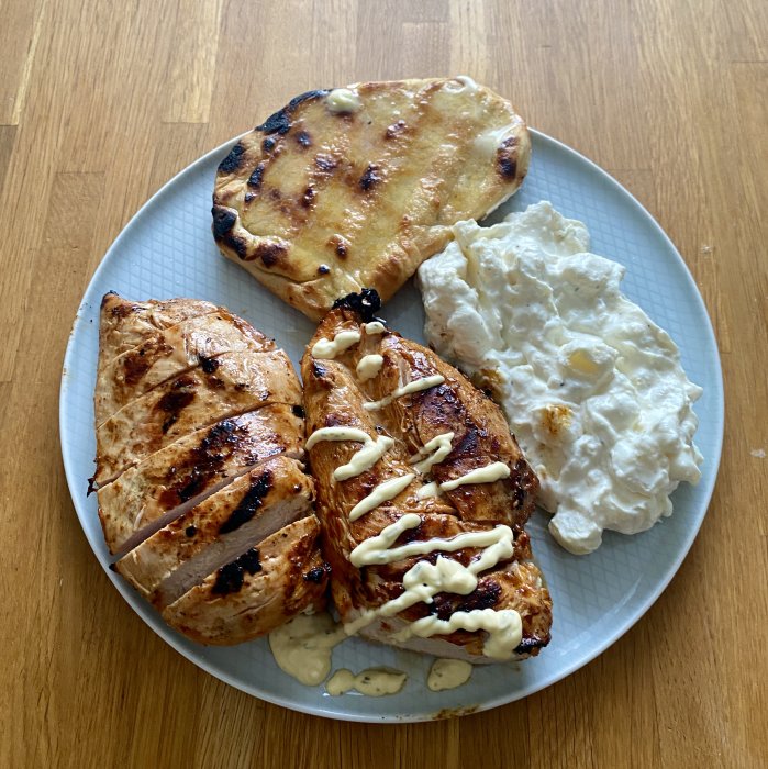 Grillad kycklingfilé med marinad, potatissallad och hembakat bröd på en tallrik.