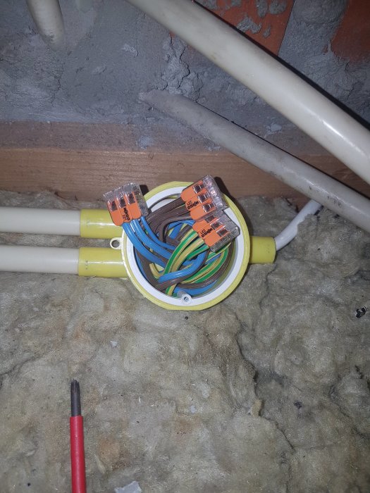 Elektriska kablar i kopplingsdosa med färgkodade skarvar och isolering, på en byggarbetsplats.